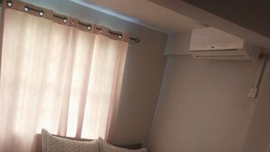 A bedroom with a bed, curtains, a wall-mounted air conditioner, and a small rug. - Charming 2-bedroom apartment in Babonneau with WiFi, AC (Babonneau)