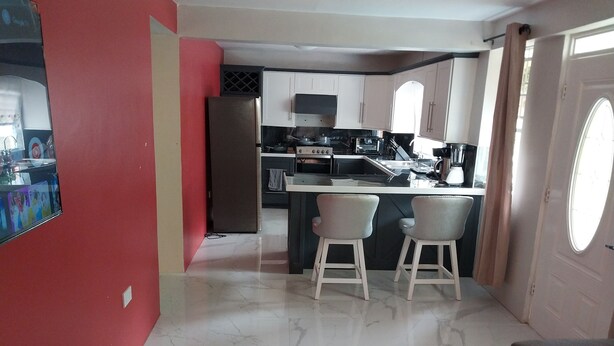 A compact kitchen with a central island, white cabinets, and a red accent wall. - Charming 2-bedroom apartment in Babonneau with WiFi, AC (Babonneau)