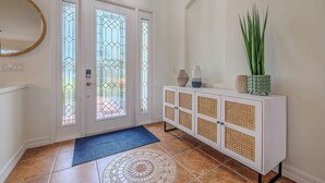 Un pasillo con una puerta blanca, un felpudo azul, un aparador blanco y un espejo grande en la pared.