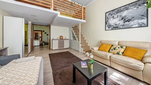 Un apartamento moderno con habitación tipo loft, sala de estar con sofá y mesa de centro, y una escalera que lleva al piso superior.