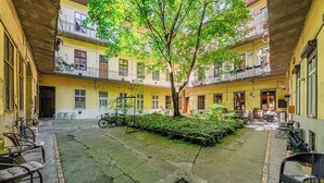 Un patio central con un árbol, rodeado de edificios amarillos con balcones y zonas de estar al aire libre.