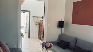 Un soggiorno con un divano grigio, un tavolino da caffè bianco con un vaso di fiori, una lampada a sospensione in vimini e un addobbo rosso al muro.
