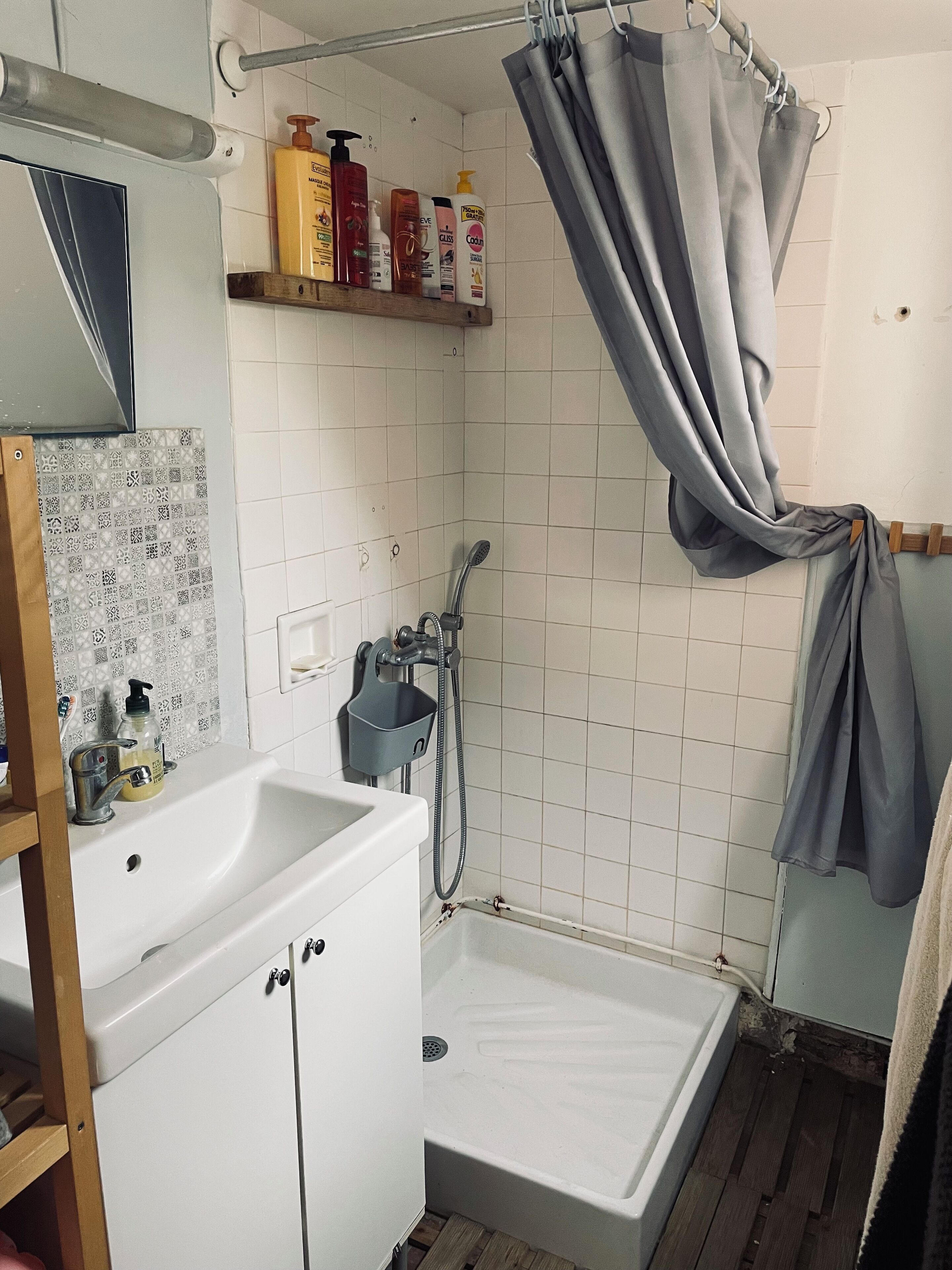 Une salle de bain avec un lavabo blanc, une douche et une baignoire. On trouve des articles de toilette sur une étagère au-dessus du lavabo.