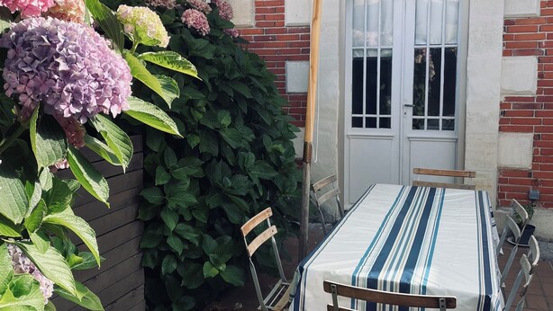 Patio esterno con tavolo e sedie, zona coperta con tetto bianco e parete in mattoni con una finestra.