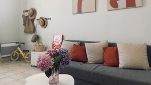 Un soggiorno con un divano grigio, un tavolino da caffè bianco e un vaso con fiori. Si notano due opere d'arte appese al muro, un cappello e una bicicletta sullo sfondo.