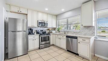 A modern kitchen with stainless steel appliances, white cabinetry, and a tiled floor.