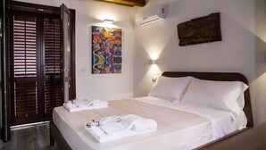A hotel room with a bed, white linens, a colorful painting on the wall, and a wooden ceiling. - House Alley St. John (Palermo)
