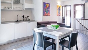 A modern kitchen with white cabinets, a dining table with black chairs, and a green bowl on the table. - House Alley St. John (Palermo)