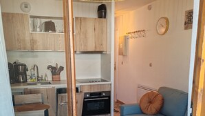 A compact kitchen with a stove, oven, and coffee maker. A blue sofa with a brown pillow is in the living area.