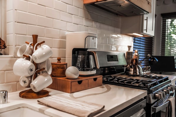Una cocina moderna con cafetera, hervidor y una pila de tazas blancas sobre la encimera.