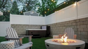 Un espace extérieur aménagé en terrasse, avec un foyer, deux fauteuils Adirondack, une table et un barbecue.