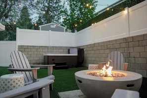 Un espace extérieur aménagé en terrasse, avec un foyer, deux fauteuils Adirondack, une table et un barbecue.