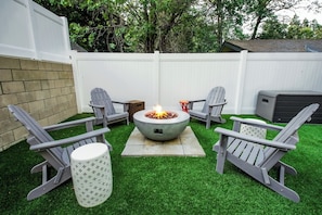 Un patio trasero con un brasero, cuatro sillas Adirondack y una mesa pequeña.