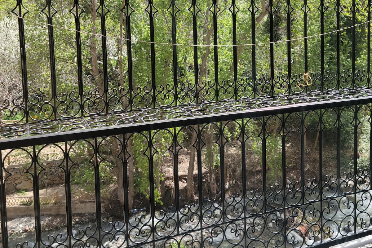 A balcony with a wrought iron railing overlooking a mountainous landscape with trees.