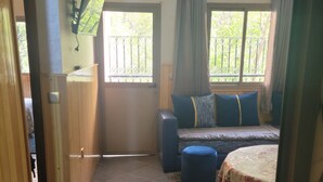 A room with a bed, a sofa, a TV mounted on the wall, and a window with a view of greenery. - ATLAS OURIKA HOME (Sti Fadma)