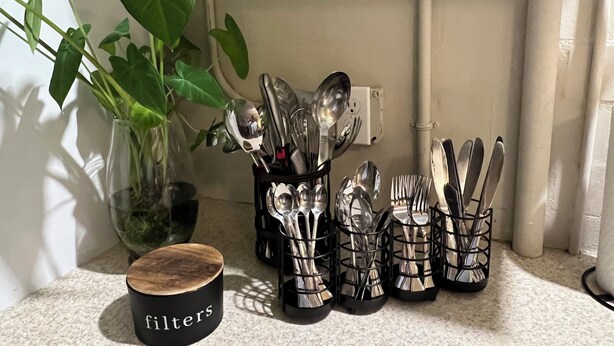 A kitchen counter with a plant, a wooden container labeled "filters," and several utensil holders.