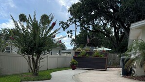 A concrete driveway leading to a gated entrance with a wooden fence and a large tree.
