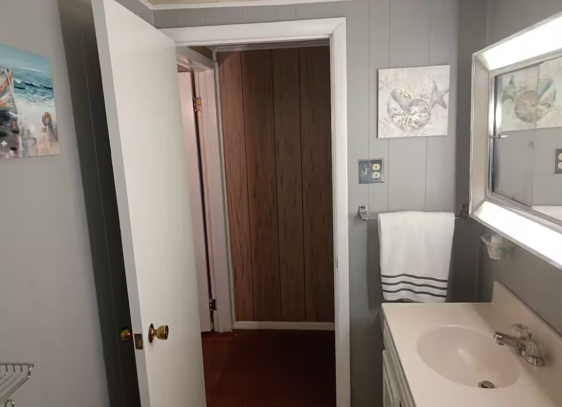 A bathroom with a sink, mirror, towel, and wooden door leading to another room.