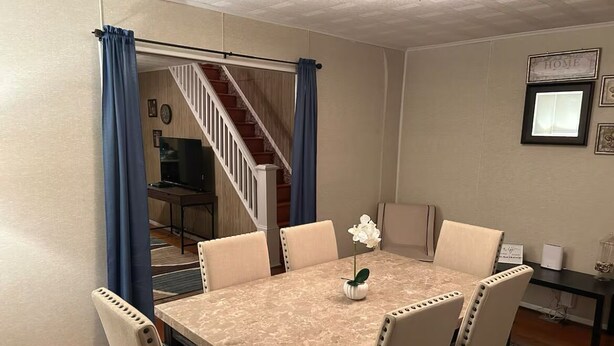 Un comedor con una mesa de mármol, seis sillas, un jarrón con una flor, una escalera que lleva a otra habitación y un letrero que dice 'HOME' en la pared.