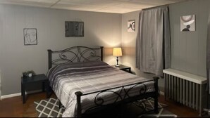Un dormitorio con cama, mesita de noche, lámpara y radiador.