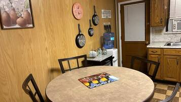 A kitchen with wooden cabinets, a round table with chairs, a water dispenser, and a clock on the wall.