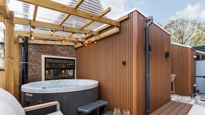 A hot tub with steps, a wooden deck, and a pergola with string lights.
