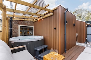 Un bain à remous avec des marches, une terrasse en bois et une pergola illuminée de guirlandes lumineuses.