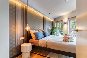 A modern bedroom with a bed, bedside lamps, a plant, and a window. - Luxury boutique stay with sauna & jacuzzi on the harbor of Medemblik! (Medemblik)
