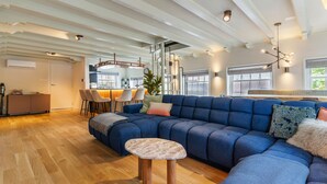 A modern living room with a blue sectional sofa, a small round table, and a dining area with chairs.