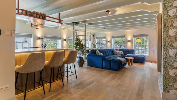 A modern kitchen with a bar area, a blue sofa, and a large window.