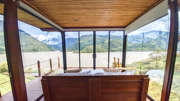 Un banc en bois, placé dans un espace extérieur abrité, d’où l’on peut admirer un lac et des montagnes.