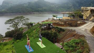 Two people practicing yoga on a green mat with a view of a lake and mountains in the background.