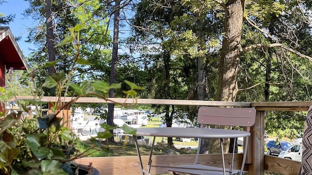 Eine Holzterrasse mit Tisch und Stühlen, umgeben von Bäumen und mit Blick auf Wohnmobile im Hintergrund.