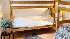 Ein Stockbett mit weißer Bettwäsche, ein gewebter Korb mit einer Pflanze und ein grauer Teppich auf dem Boden.