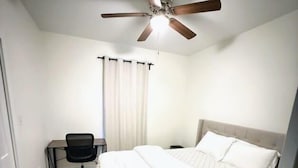 A bedroom with a bed, a desk, a chair, a ceiling fan, and a window with curtains. - Newly Renovated 2 Bedroom - B (Durham)