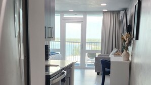Une cuisine moderne dotée d’appareils électroménagers en acier inoxydable, un coin repas avec une table et des chaises blanches, et un balcon offrant une vue sur la mer.