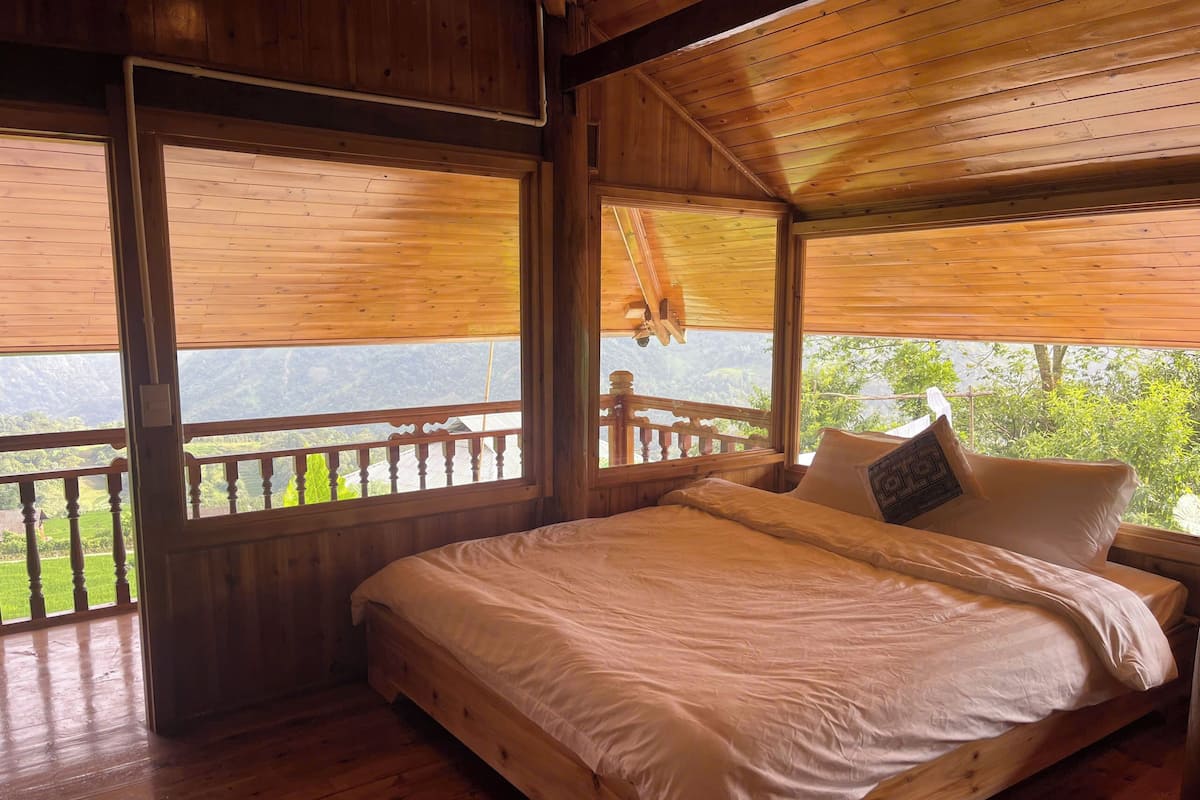 Une chambre dans un chalet en bois, avec un lit, de grandes fenêtres et un balcon donnant sur un paysage montagneux.