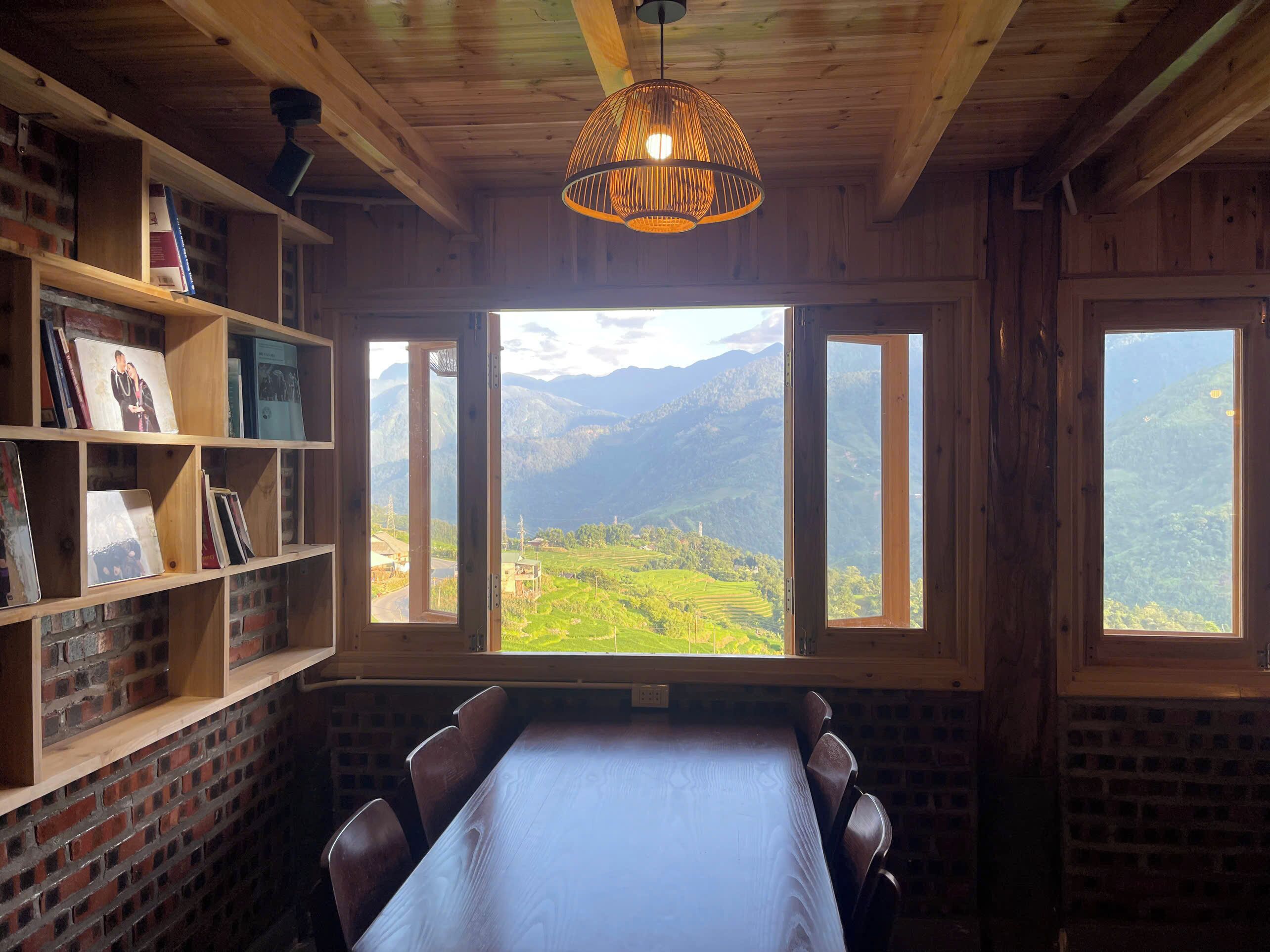 A room with a wooden table and chairs, a bookshelf, and a large window with a mountain view.