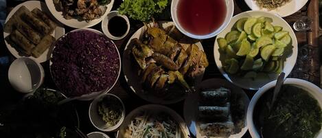 A table with various dishes, including a bowl of purple rice, a plate of grilled chicken, and several bowls of soup.