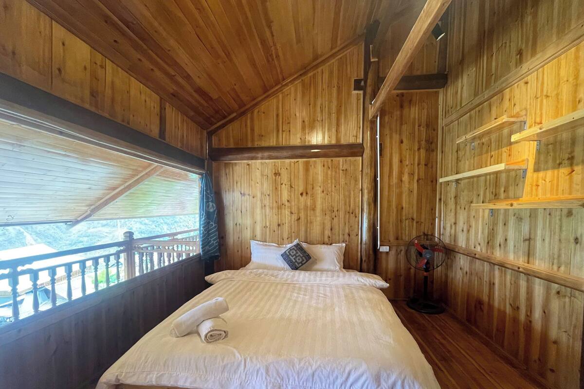 Une pièce en bois avec un lit, une fenêtre et un ventilateur.