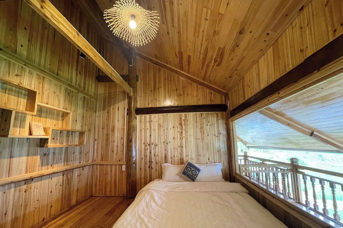 Une pièce de cabane en bois comprenant un lit, des étagères et une fenêtre donnant sur un paysage agréable.