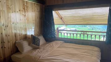 Habitación de cabaña de madera con cama, ventana con vista a campos verdes y balcón.