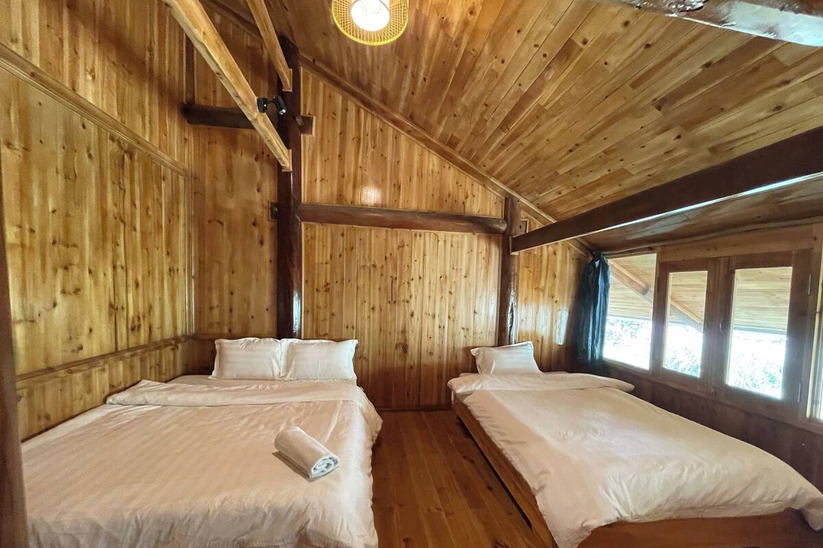 Une cabane en bois avec deux lits, un plafond en pente et de grandes fenêtres.