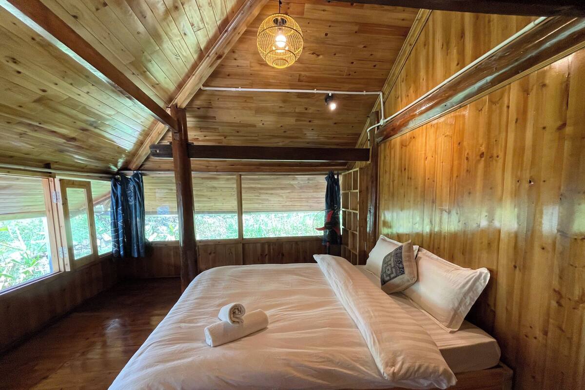 Une chambre dans une cabane en bois, avec un lit, un luminaire suspendu et des fenêtres avec des rideaux.