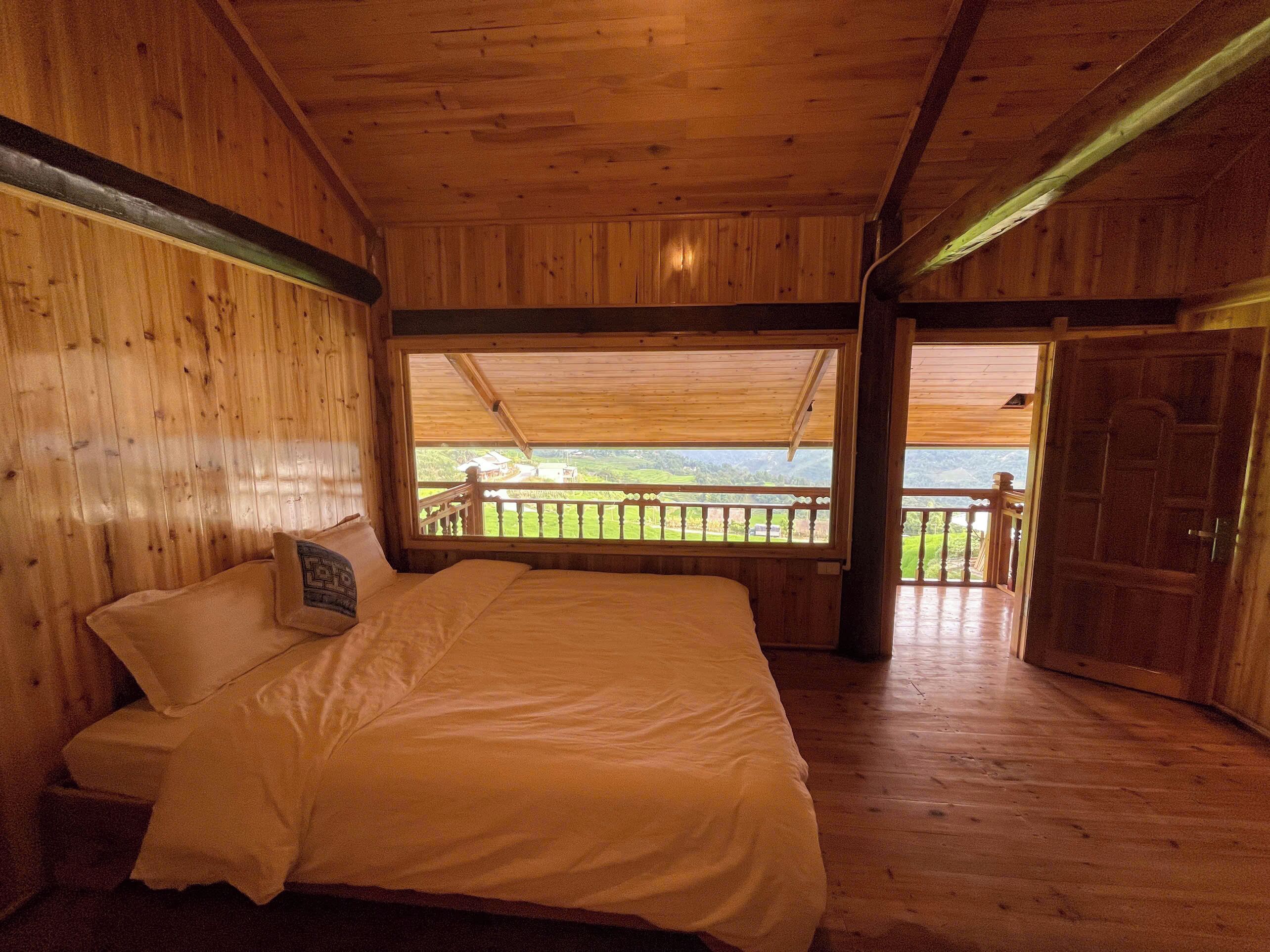 Habitación de cabaña de madera con una cama, un ventanal con vistas a un paisaje verde y un balcón.