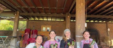 Four people seated under a wooden roofed structure with brick walls, holding wrapped food items.