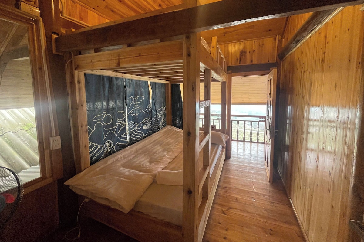 Une chambre dans un chalet en bois, avec des lits superposés, une fenêtre donnant sur un paysage agréable et un ventilateur.