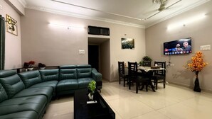 A living room with a sectional sofa, a dining table with chairs, a TV mounted on the wall, and a ceiling fan.