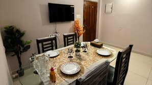 A dining room with a glass table, chairs, a television mounted on the wall, and a door.