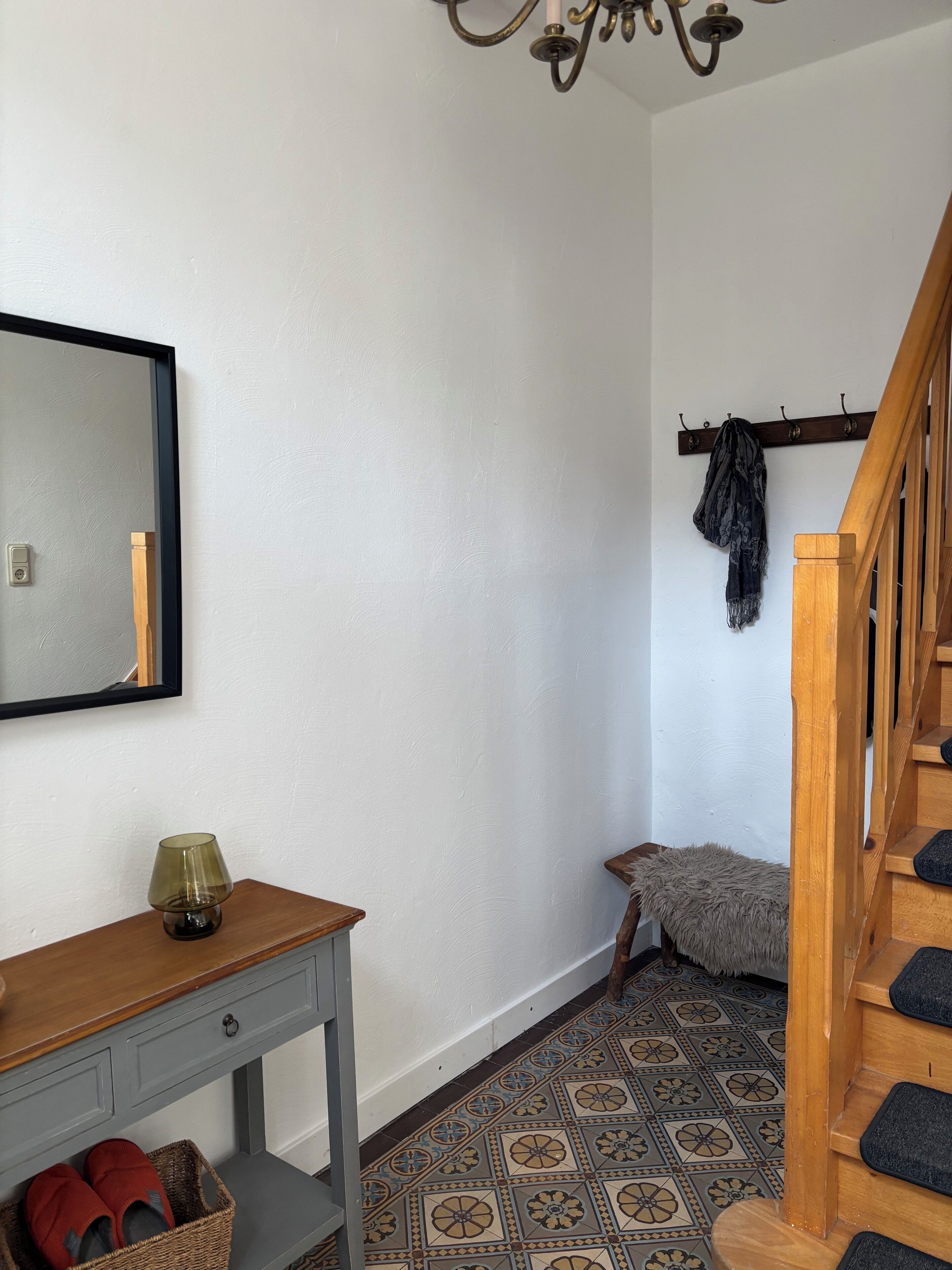 A room with a wooden desk, a mirror, a coat rack, a patterned floor, and a staircase.